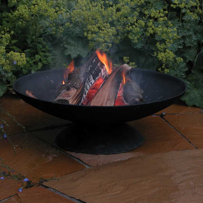 Flaming logs in fire bowl standing on wet patio in front of alchemilla
