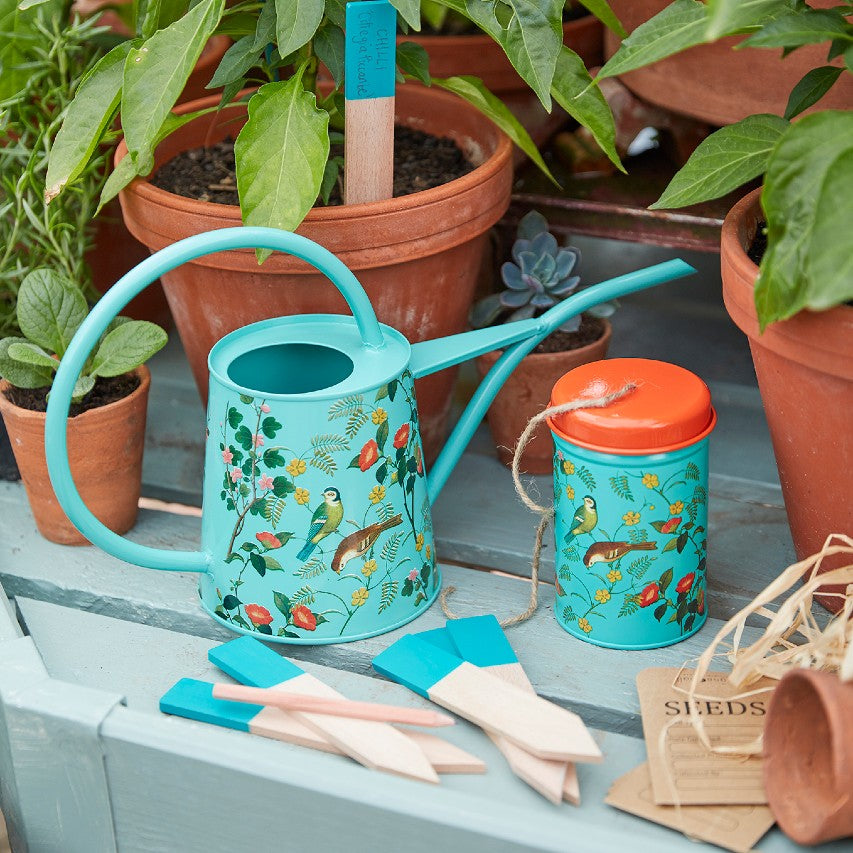 Flora and fauna watering can with twine and wooden labels on greenhouse bench next to terracotta pots
