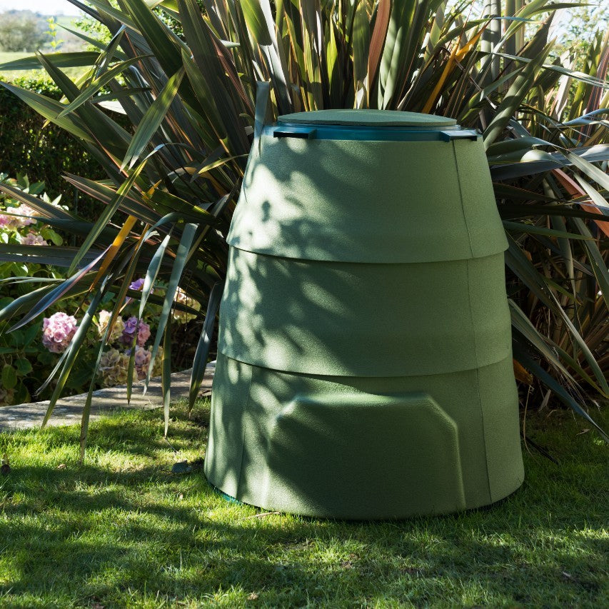 Green Johanna garden composter with winter jacket standing on grass in front of phormium