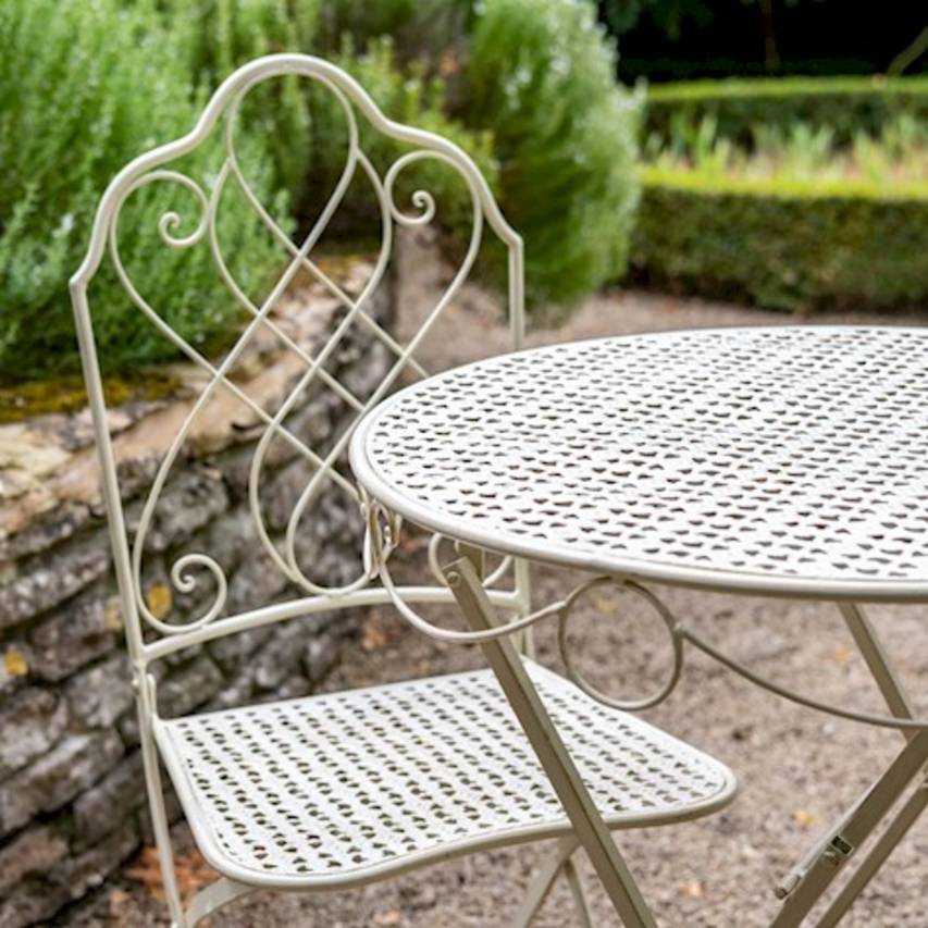 Close-up of cream Avalon bistro set with a low dry stone wall in the background and rosemary plants growing above the wall.