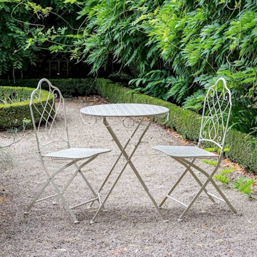 Cream Avalon 3-piece bistro set placed on a gravel path, with box hedging and flowering wisteria in the background.