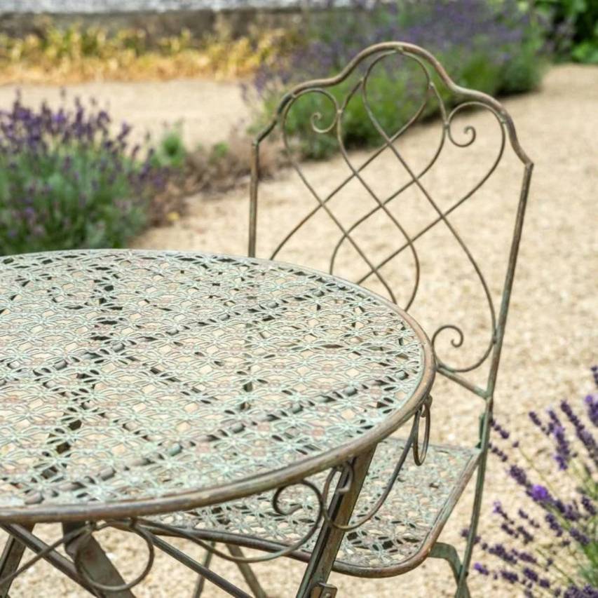 Close-up of green rust Avalon bistro table and chair showcasing decorative metalwork and weathered finish.