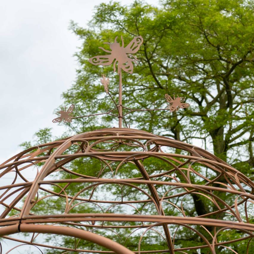 Close-up of the bee sculpture atop the bee gazebo, with a tree and blue sky in the background.