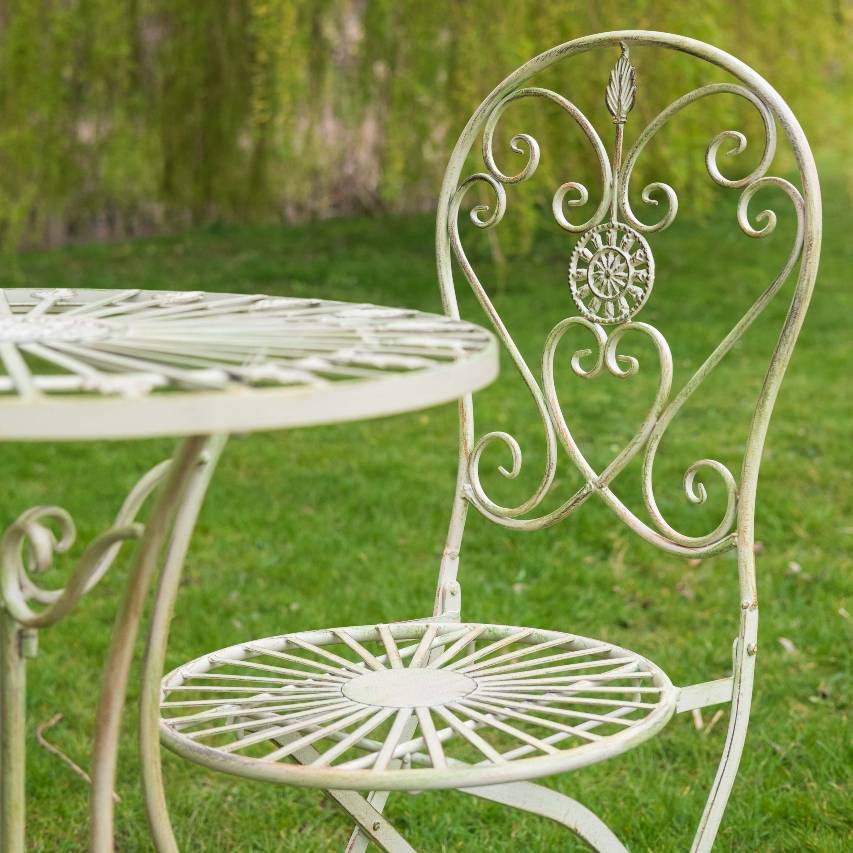 Close-up of cream Blaisdon bistro table and chair placed on grass with a willow tree in the background.