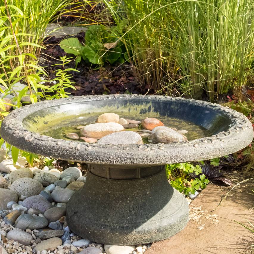 Coniston bird bath with pebbles in front of grass border