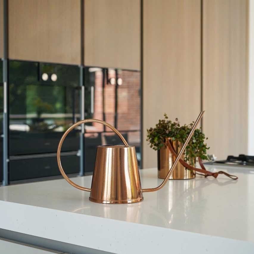 Indoor Kensington copper watering can on kitchen surface next to brass hanging planter with plant