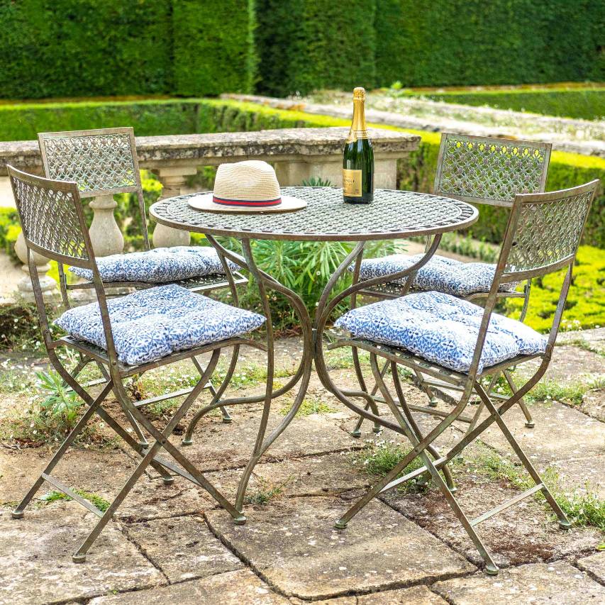 Ascalon Marlborough 5-piece bistro set in antique blue rust with seat cushions, styled with a champagne bottle and sunhat.