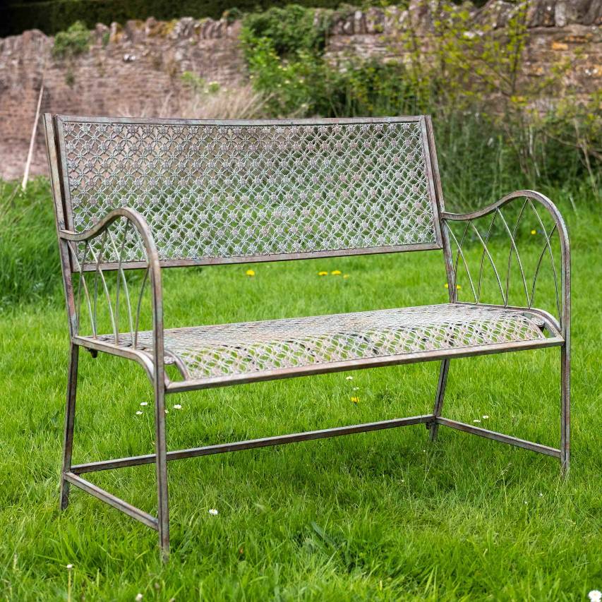 Ascalon Marlborough bench in antique blue rust standing on grass with stone wall in background.