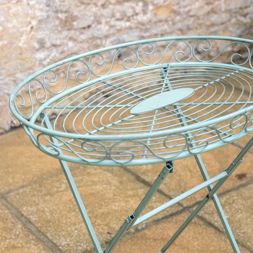 Close-up of green Woodland butler's table on a patio, with a stone wall in the background.