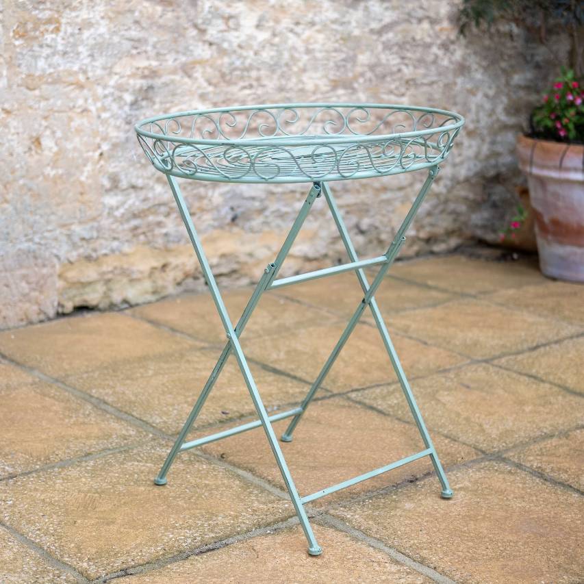 Green Woodland butler's table on a patio, with a stone wall in the background and a terracotta pot of fuchsia in the corner.